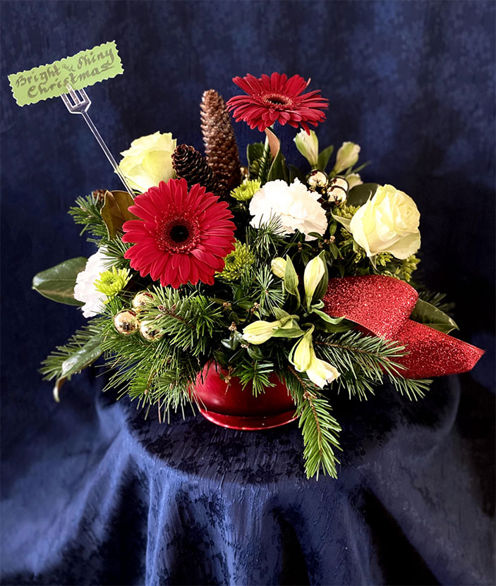 Bright and Shiny Christmas $75 Red or gold shiny compote, evergreens of white pine, boxwood, magnolia, green roses, green mini hydrangea, red gerbera daisies, white alstroemeria, white carnations, green.