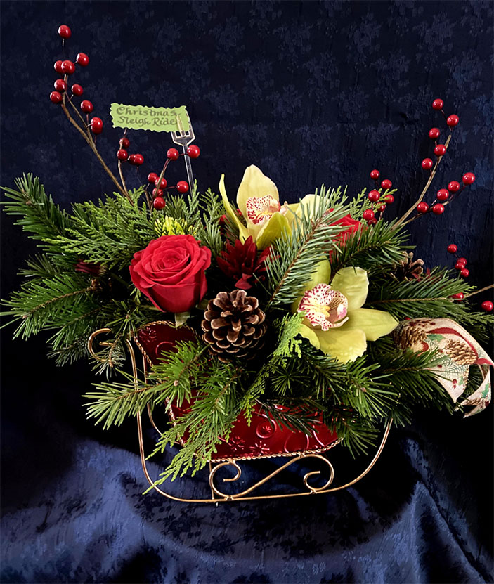 Christmas Sleigh Ride $79 Small red and gold sleigh, seasonal greens of fir and cedar, green cymbidium, orchids, red roses, red pom-poms, red berries and seasonal ribbon tails.