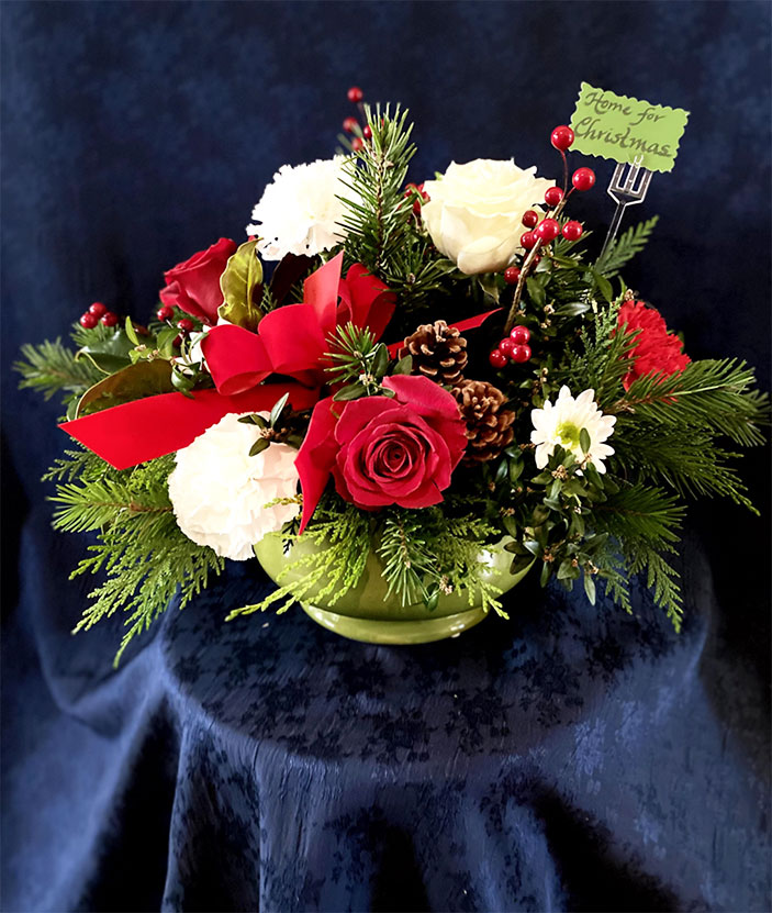Home for Christmas $75.50 Large green or red bowl, greens of fir, boxwood, cedar and magnolia, red and white roses, red and white carnations, white pom-pos, berries, pine cones and a red velvet box.